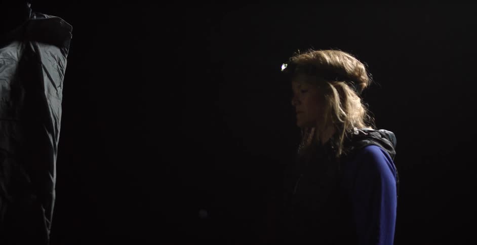 A man unrolls a black tarp in the dark while a woman watches
