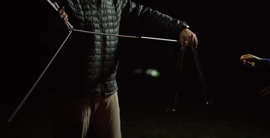 A man and a woman are setting up a tent at night
