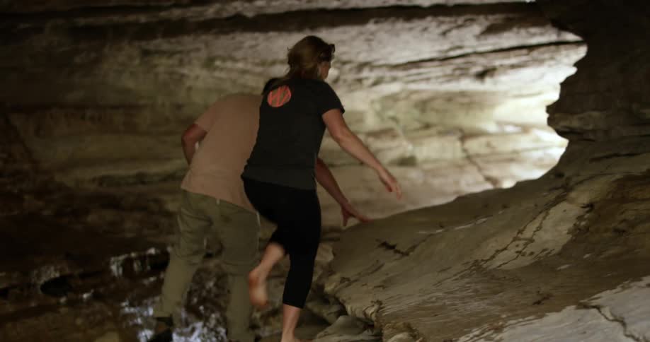 Man and woman walking over a small stream in a cave
