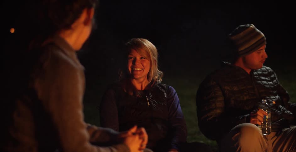 Campers laugh and sit near a campfire