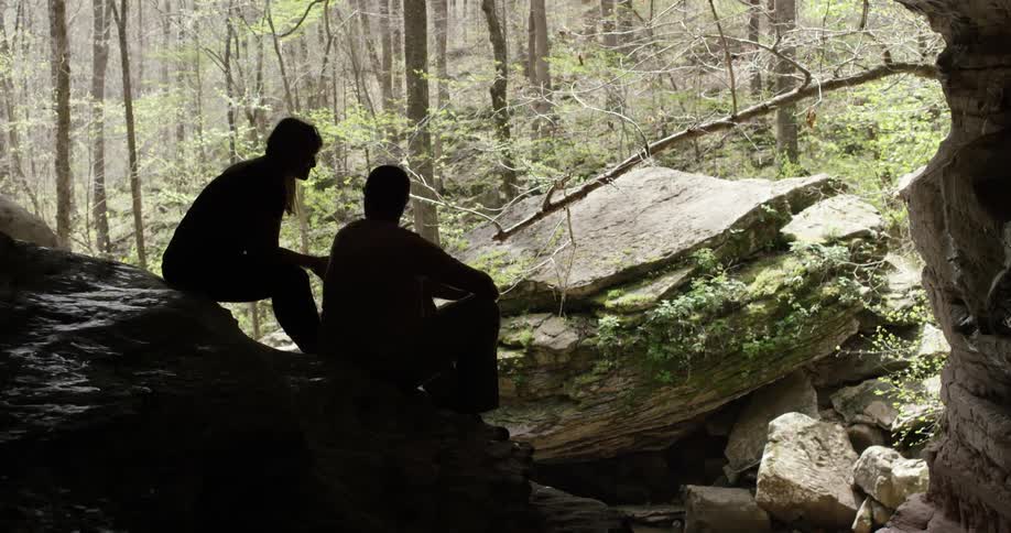 Two people sit on a rock in the forest