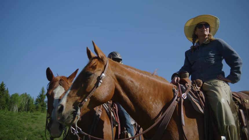 Two female ranchers sit on horse and take in their surroundings