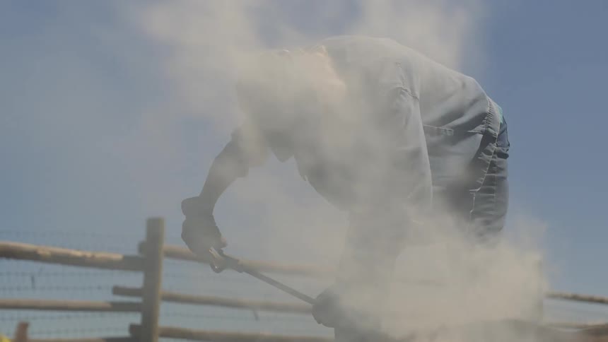 Woman with a metal rod emitting smoke towards a lying animal