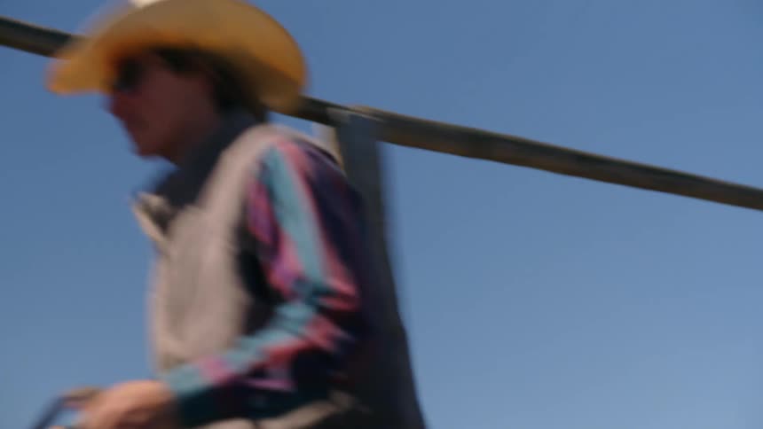 Two cowboys riding horses through a wooden gate