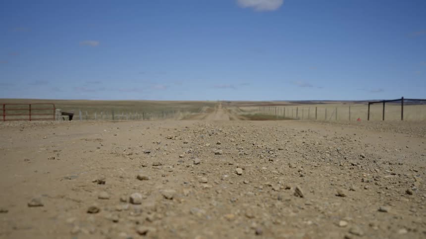 Dirt road passes fenced fields in the rural countryside