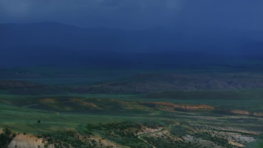 Aerial landscape of greenish mountains and plateau against a cloudy blue sky