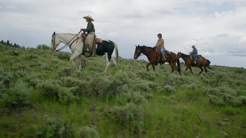 People ride horses up a slight slope on an overcast day