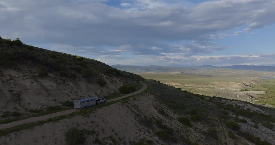 A truck towing a trailer travels along the mountain road