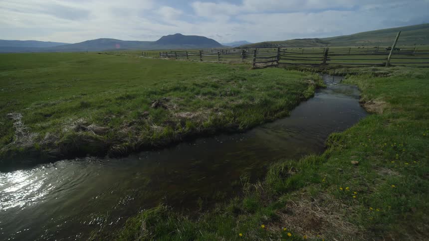 Stream flows past a fenced pasture on a cloudy day
