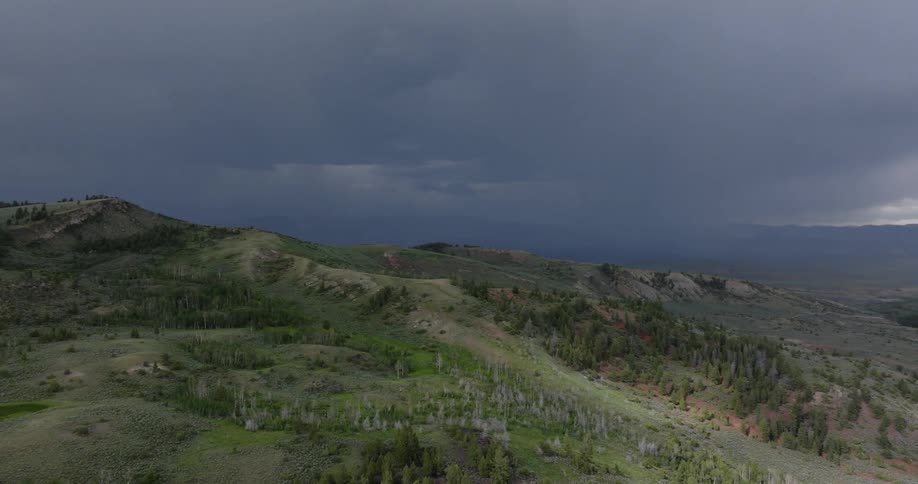 Dark storm clouds gather above rolling hills covered in green vegetation