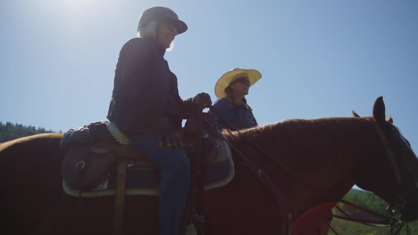 Two female ranchers carry on a conversation while sitting on horses outdoors