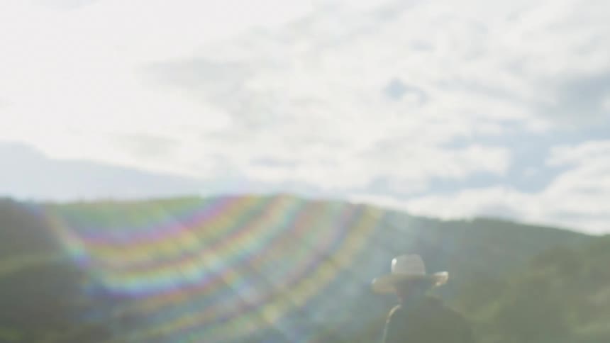 Woman rides a horse past green hills on a cloudy day