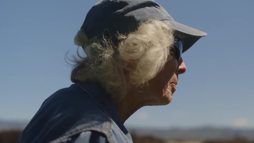 A side profile of a woman with white hair wearing a baseball cap against a clear sky