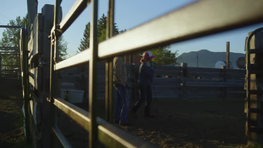 Two individuals in a rural setting one opening a metal gate while the other stands nearby