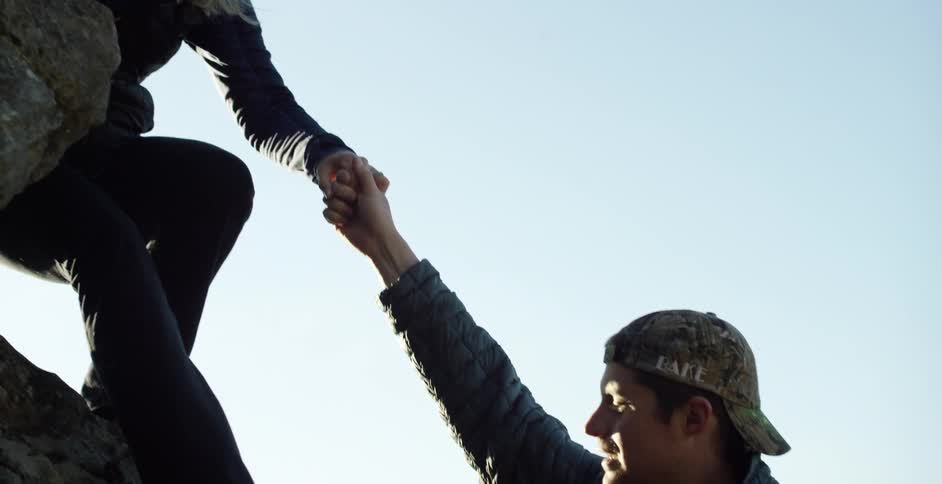 Woman holding a man's hand as she climbs down a rocky cliff