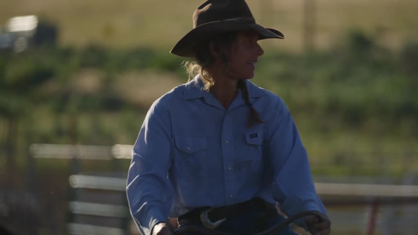 A female rancher smiles as she rides a horse around inside an enclosed area