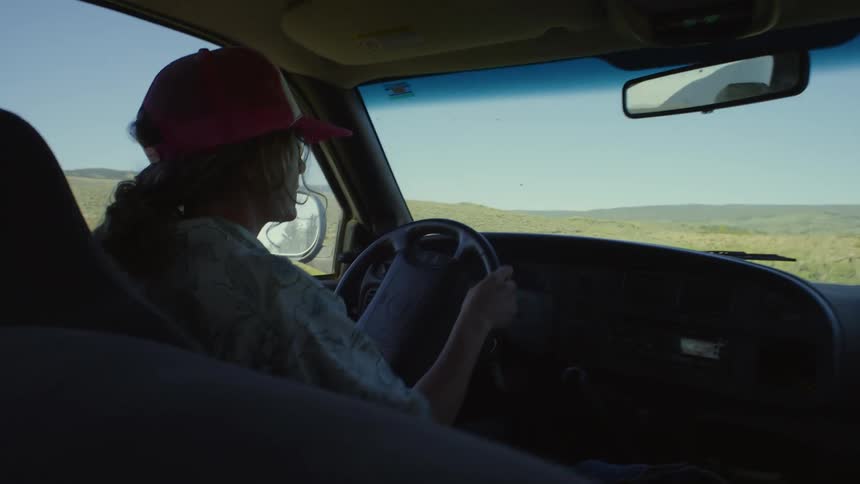 Woman driving a pickup truck in a natural environment with mountains in the background