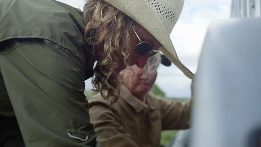 Women change the tire of a livestock trailer while their dog walks around