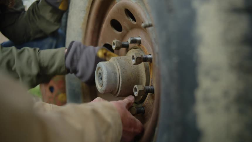 Hands of two people removing the bolts from a vehicle wheel