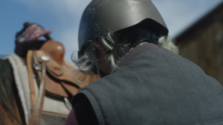 An old woman adjusts equipment on a horse