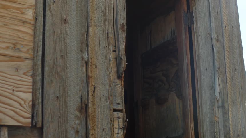 Two women leave a wooden storage shack carrying saddles