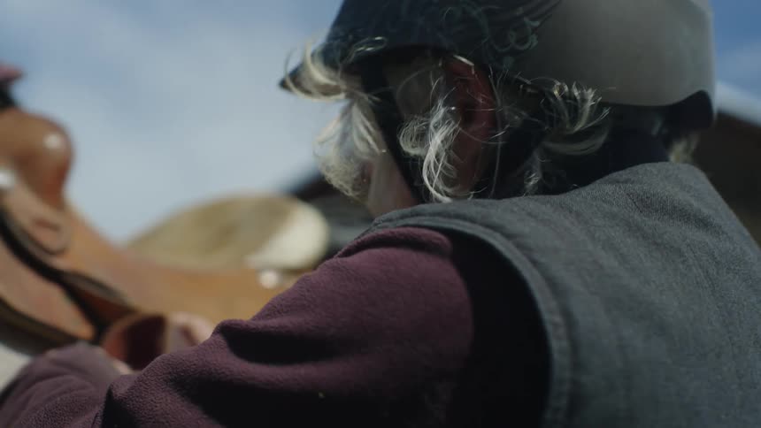 Woman adjusting a horses harness while wearing a protective helmet
