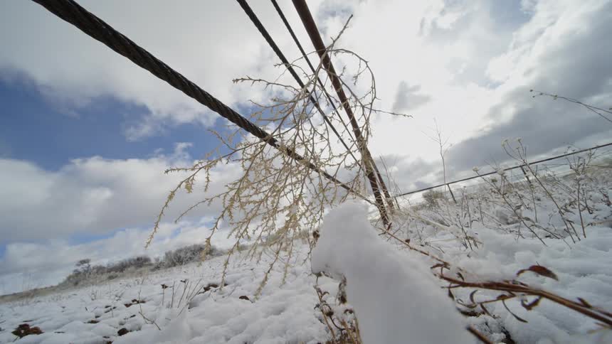 Low angle view of a snow covered landscape with a meal fence under cloudy skies