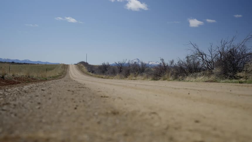 A dirt road stretches through a dry landscape with sparse vegetation under a clear sky