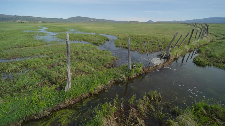 A creek flowing across a wire and wood fence