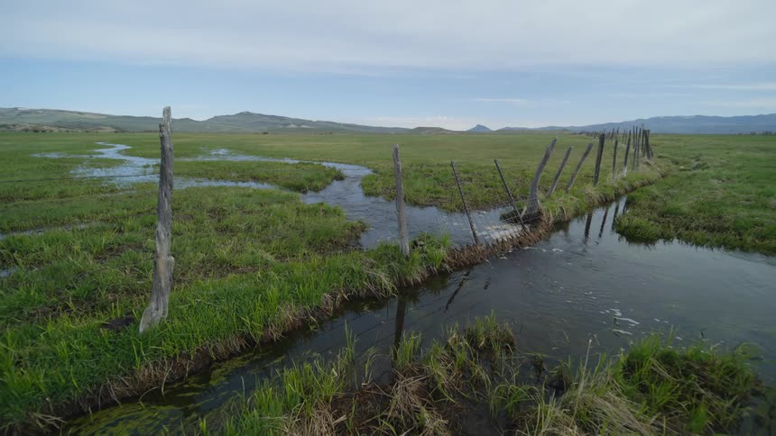 A river running through a grass field with a wooden and wire fence
