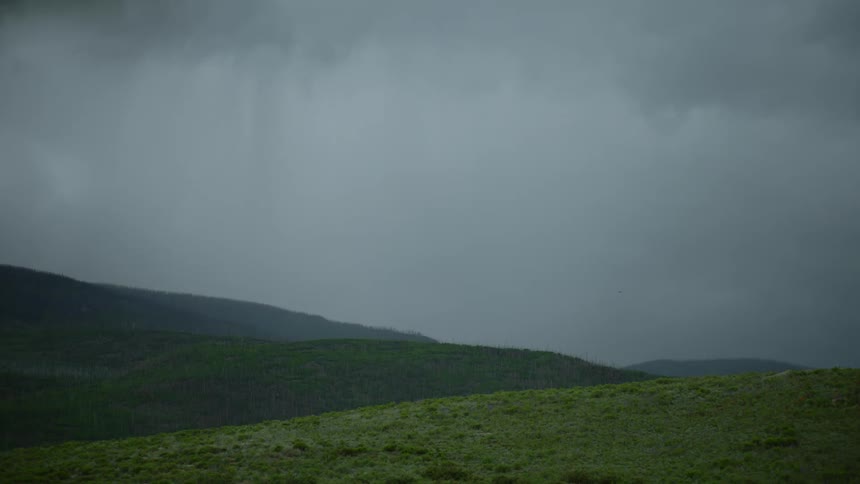 Storm clouds dump rain over a series of low mountain ranges