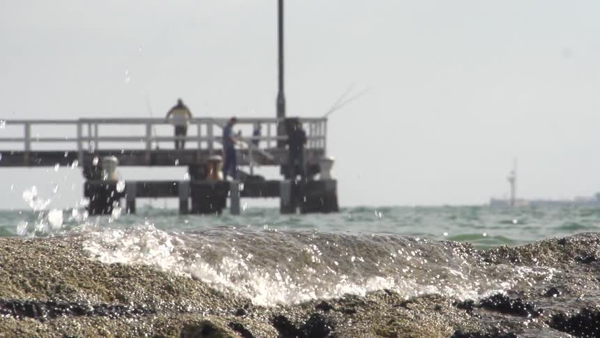 Waves crash on a beach near a pier