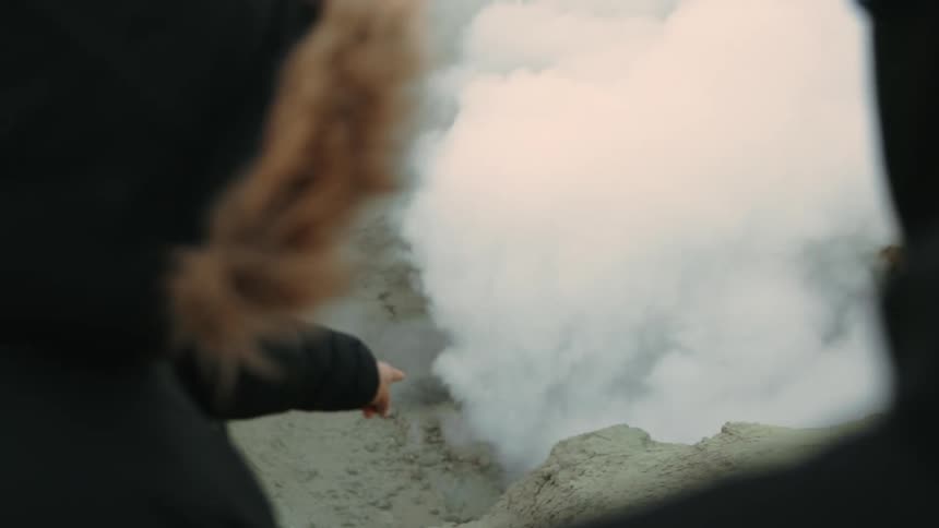 Two people watching a natural phenomenon of smoke rising from the ground