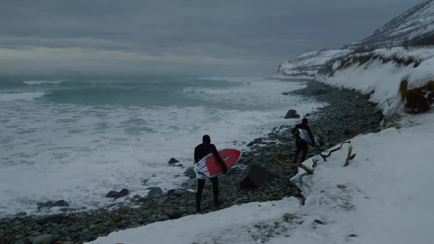 Two surfers with their boards walking between rocks by the sea