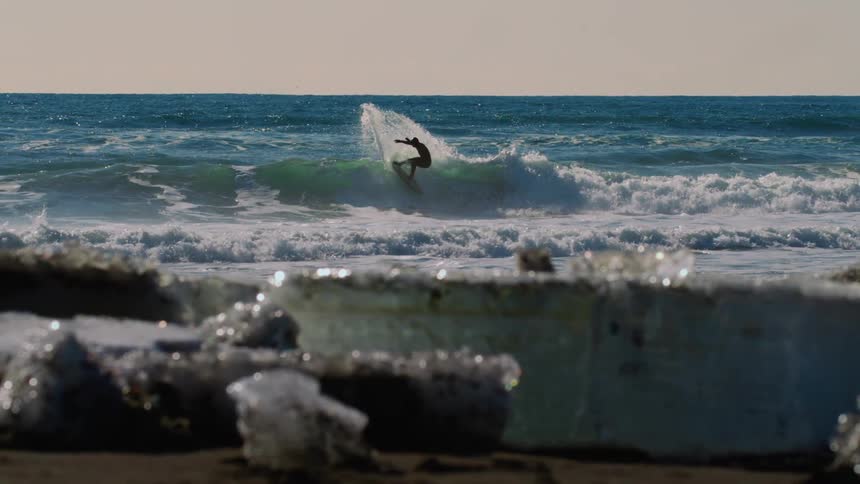Surfer riding a wave at the beach in the distance