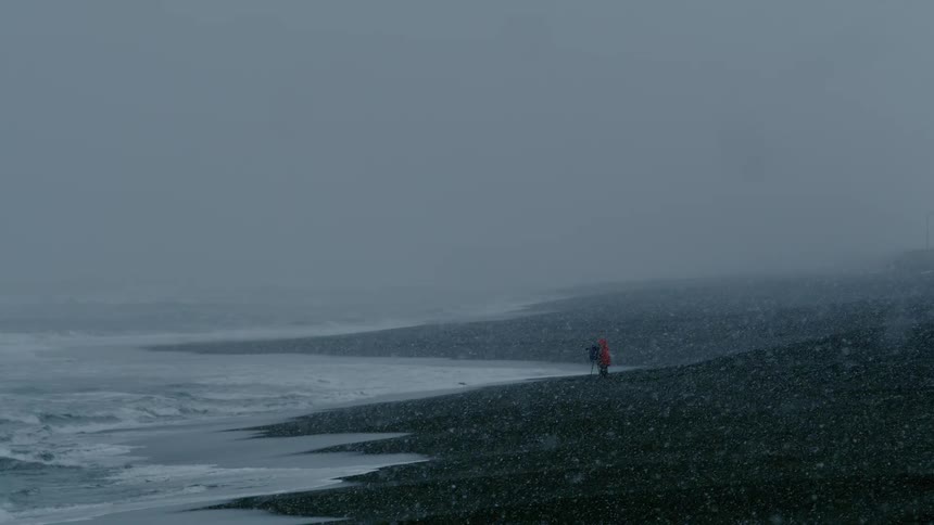 Person in an orange coat standing on the beach on a snowy day