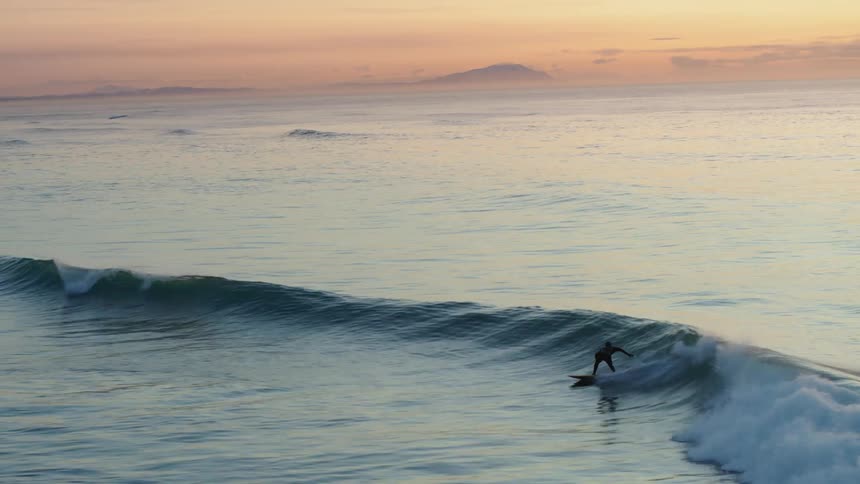 Person surfing a wave in the ocean with an orange sky
