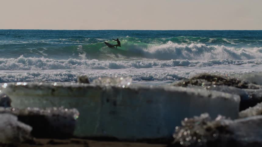 A man surfs a large foamy wave right off of a beach