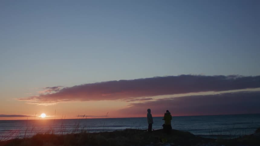 Silhouette of three people on a beach with the sun rising on the horizon