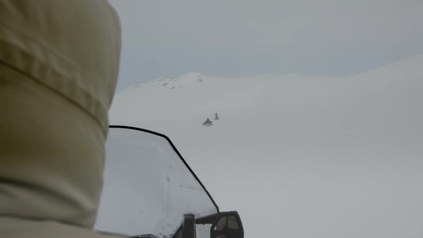 Three people ride snowmobiles up a snow covered mountain