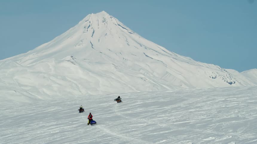 Aerial view of three people on snowmobiles traveling through snowy mountains