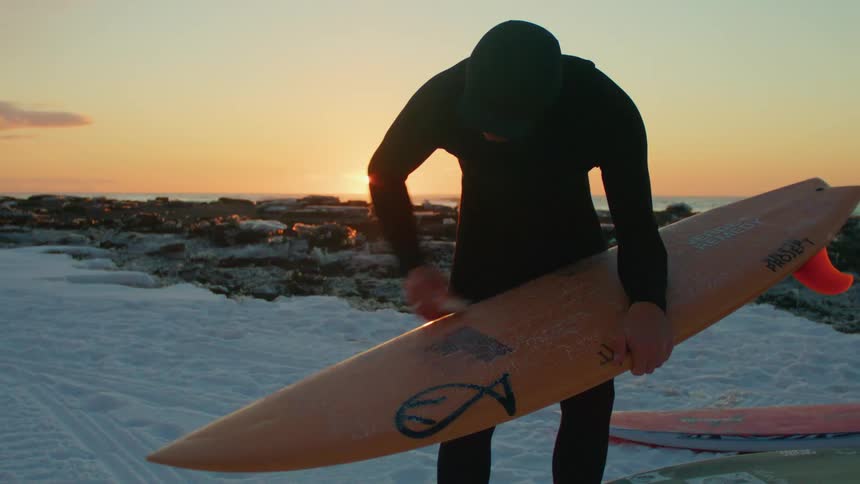A person waxing a surfboard on a beach with the sun setting in the background