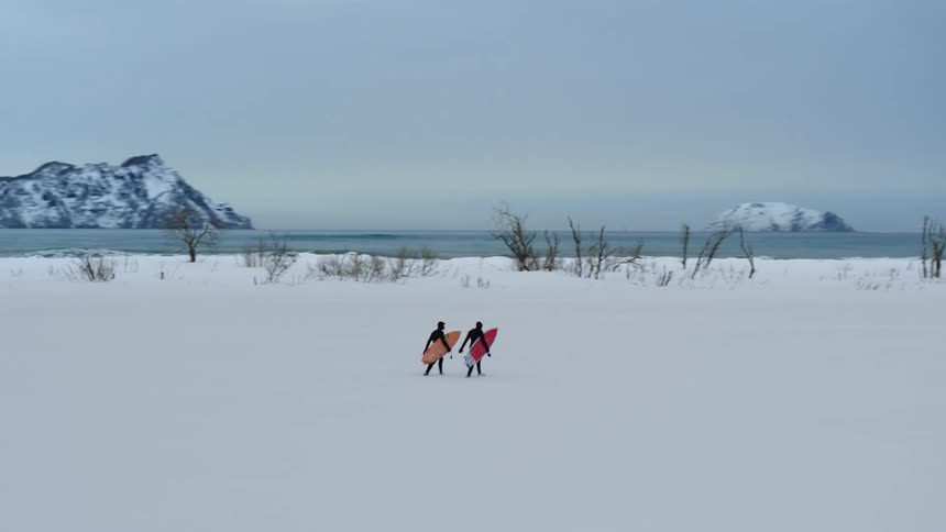 Two people carrying surfboards to a beach in winter