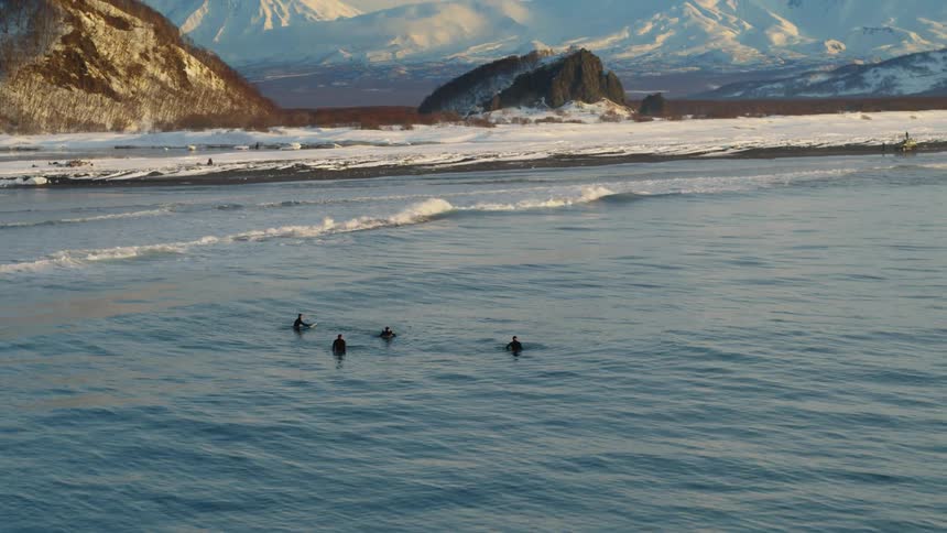 Aerial view of a group of four surfers in the sea with snowcapped mountains in the background