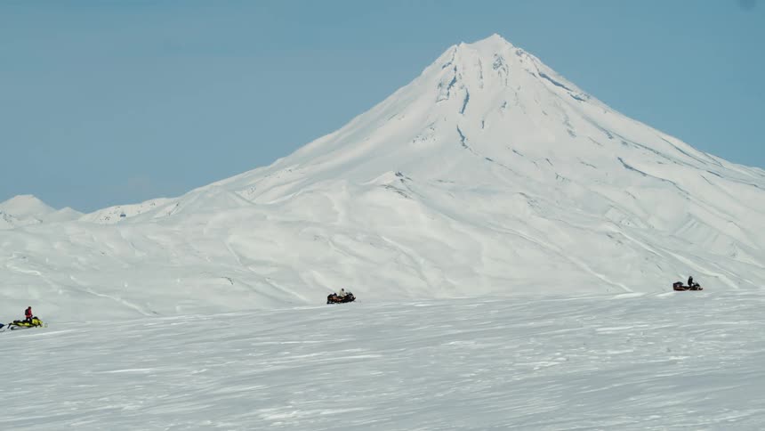 Three people riding a snowmobile with mountains in the background