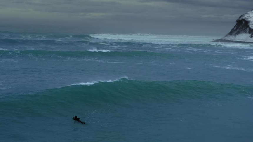 A surfer swims on his board trying to catch a wave but is pushed back by the tide