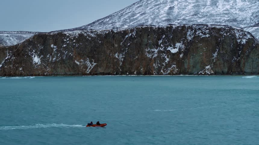 Aerial view of a boat traveling across the sea next to snowy mountains