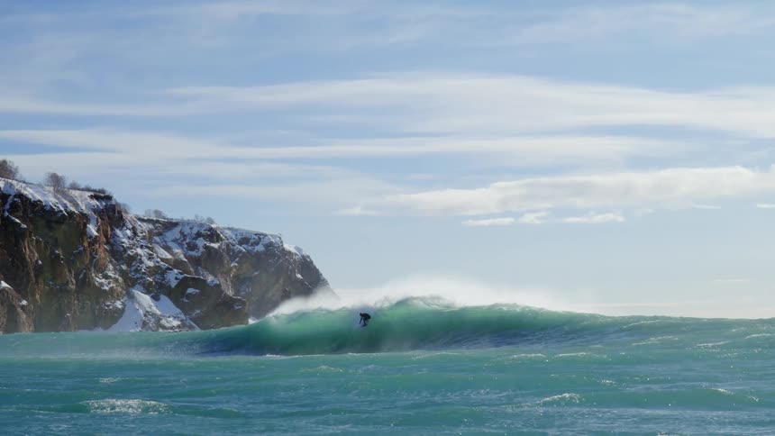 Person riding a wave and falling with snowy mountains in the background