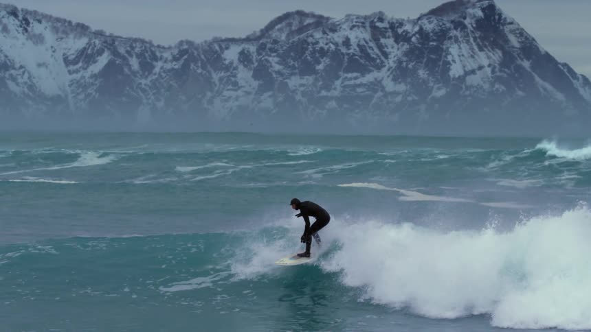 Surfer in a strong sea doing maneuvers on a wave and in the background mountains covered in snow