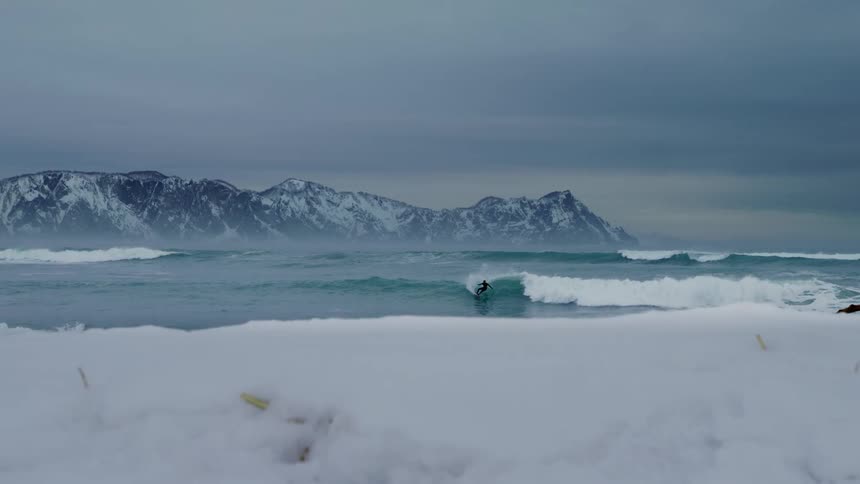 Long view of a person surfing a wave in a snowy environment